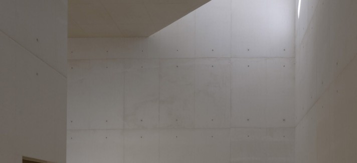 El interior destaca por sus paredes de hormigón visto, que contrastan con las puertas de madera y el suelo de grava que se extiende desde el patio exterior.