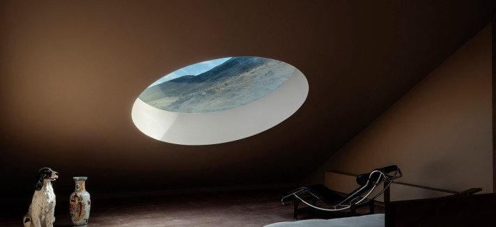 El altillo en buhardilla alberga un segundo dormitorio donde disfrutan de una claraboya circular que, situada a baja cota, enmarca las montañas lejanas.