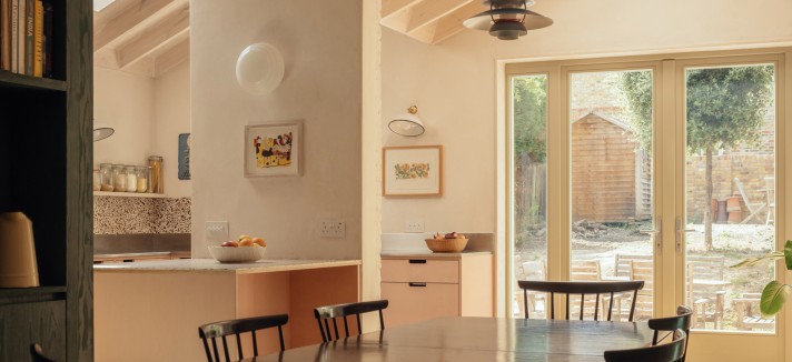 La cocina se completa con armarios y encimeras en tonos rosa pálido, superficies de acero inoxidable y un salpicadero de terrazo que introduce textura y matices.
