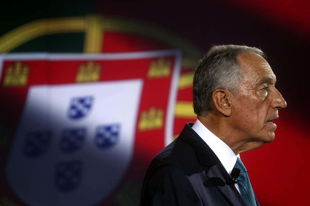 Imagem de Marcelo Rebelo de Sousa de perfil, com bandeira de Portugal como pano de fundo.