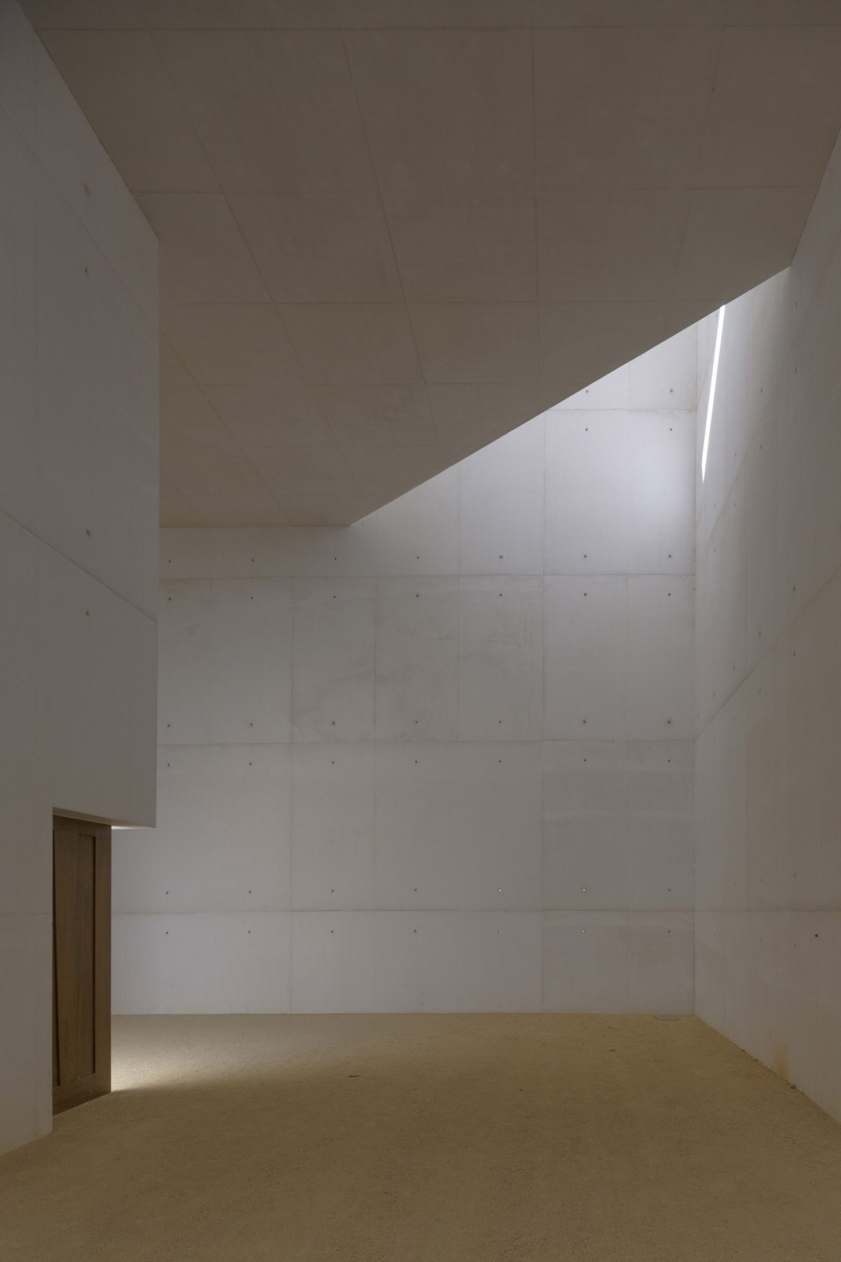 El interior destaca por sus paredes de hormigón visto, que contrastan con las puertas de madera y el suelo de grava que se extiende desde el patio exterior.
