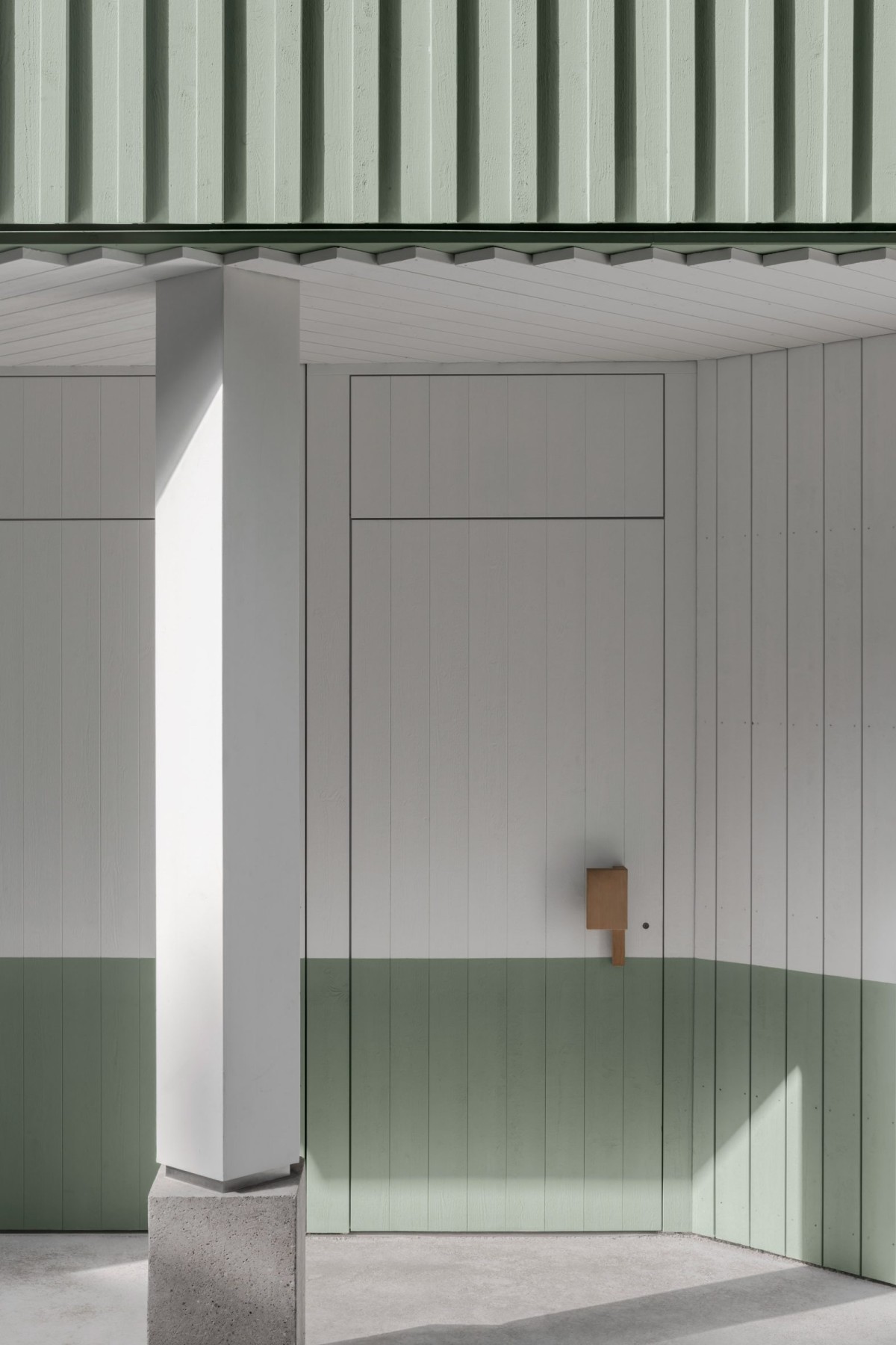 La estructura de madera está revestida con paneles verticales en un tono verde salvia que combina de manera sutil con los colores del paisaje.