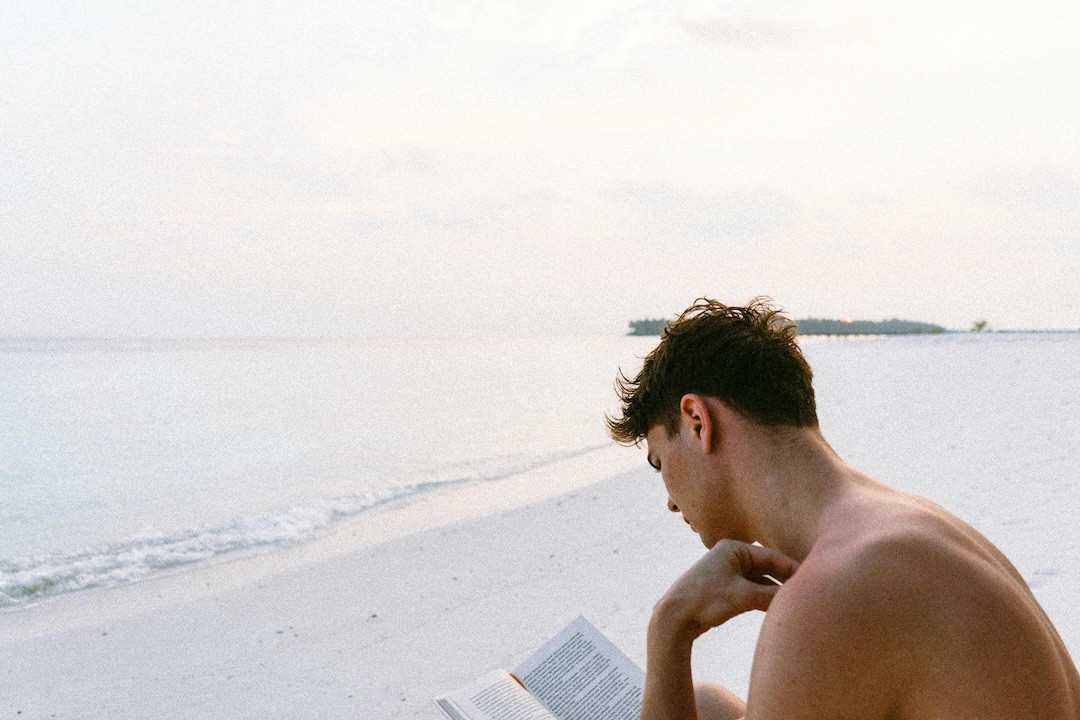 jovem rapaz a ler livro na praia