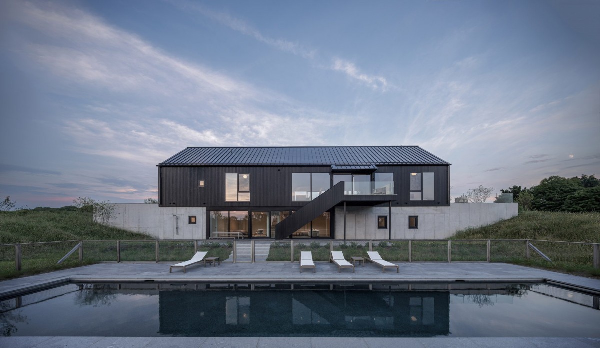 A estrutura principal, de dois andares, integra-se no terreno inclinado através de um muro de contenção em betão.