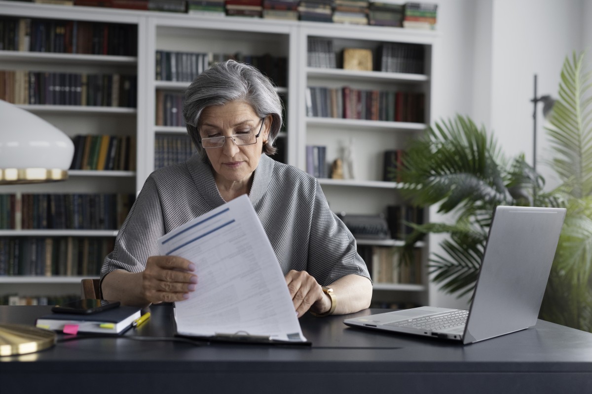 Eine ältere Dame sitzt am Computer und erledigt Papierkram.