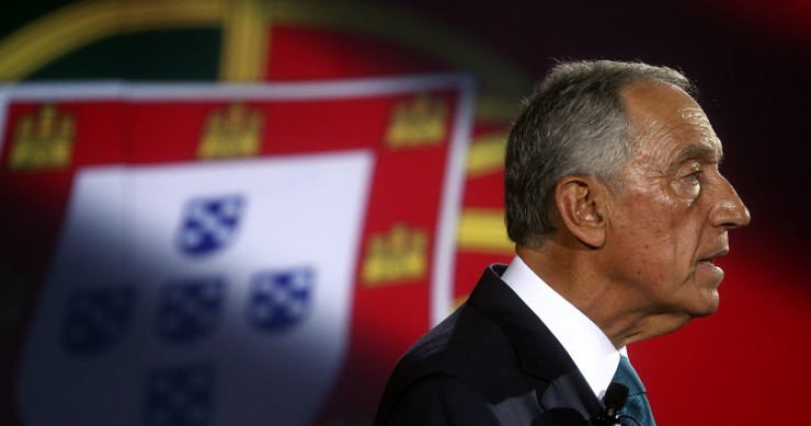 Imagem de Marcelo Rebelo de Sousa de perfil, com bandeira de Portugal como pano de fundo.