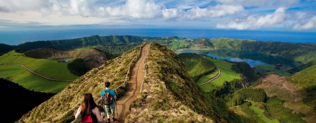 Imagem de pessoas a caminhar num trilho junto a uma lagoa, num cenário de pura natureza verde.
