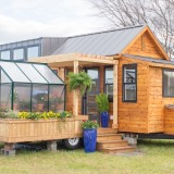 Uma minicasa sobre rodas com varanda e estufa incluídas